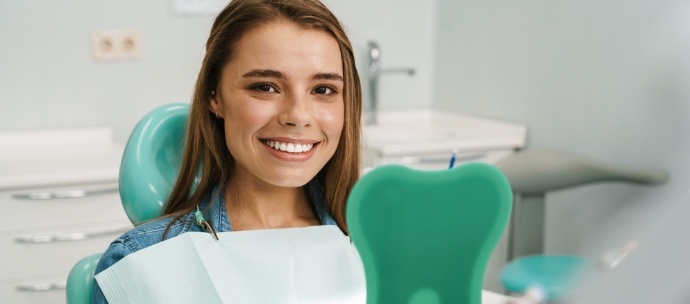 Woman sitting in dental chair smiling and holding a mirror