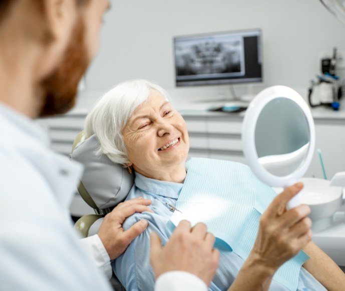 Senior woman sitting in dental chair checking smile in mirror