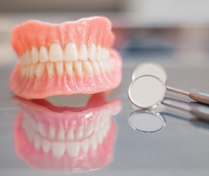 Dentures sitting on reflective surface with dental mirror