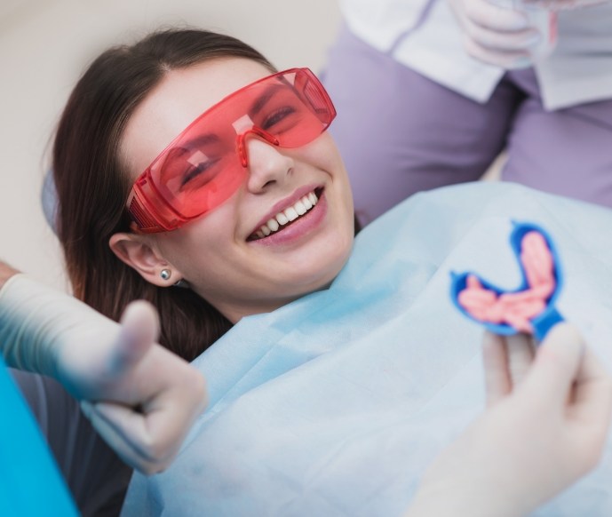 Female dental patient receiving fluoride treatment while dentist gives thumbs up