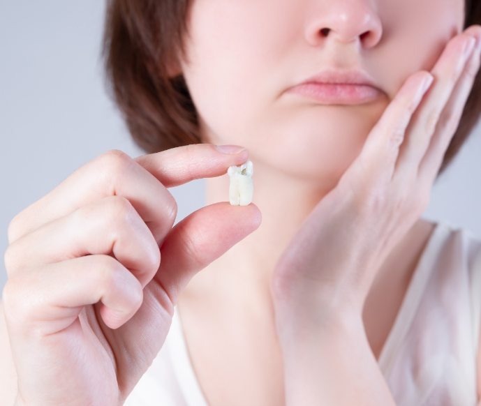 Close up of hand holding tooth while woman rubs jaw